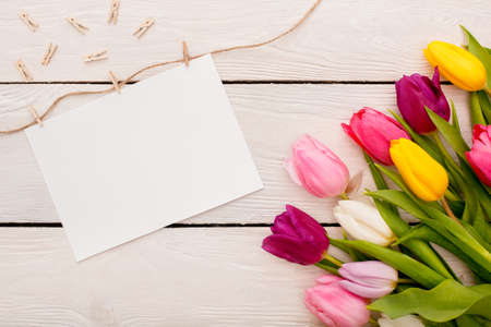 Easter traditional objects isolated on wooden floor bunch of tulips in corner and white empty paper sheet pinched with clothes pegs on ropeの写真素材
