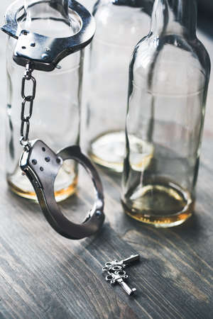 Alcohol addiction objects isolated on table no people bottle locked by handcuffs near key asking for helpの写真素材