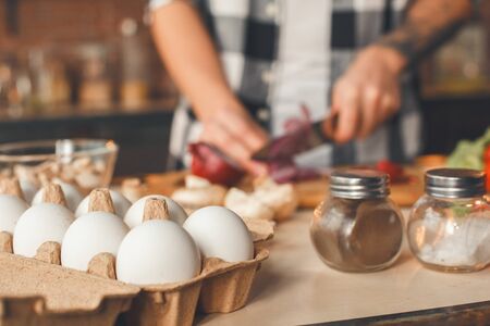 In the foreground an egg tray in the background a man makes a salad. Indoor, kitchen home interior, studio shot.の写真素材