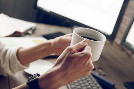 Woman holding cup of coffee in work place near computer. Indoor, studio shot. Business people concept, work in officeの写真素材