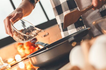 Guy pours the mushrooms into the frying pan to fry. Indoor, kitchen home interior, studio shot.の写真素材