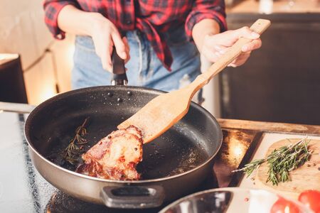 Wife fries a steak to her husband so he was strong. Indoor, kitchen home interior, studio shot.の写真素材