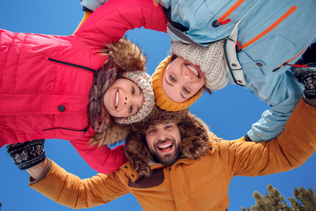 Winter vacation. Family time together outdoors hugging looking camera smiling cheerful bottom view close-upの写真素材