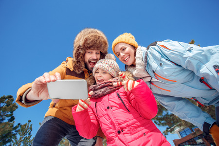 Winter vacation. Family time together outdoors taking selfie on smartphone grimacing to camera playful bottom viewの写真素材