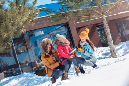 Winter vacation. Family time together outdoors sitting mother pouring hot tea from flask smiling cheerfulの写真素材