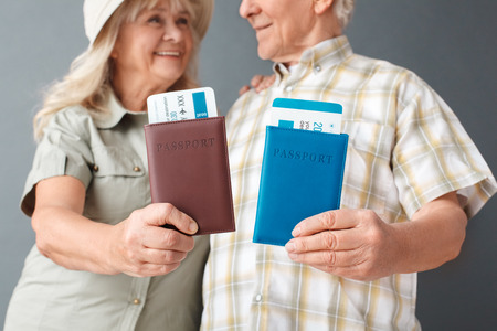 Senior tourists studio standing isolated on gray shwoing passports and tickets close-up blurred background smiling happyの写真素材