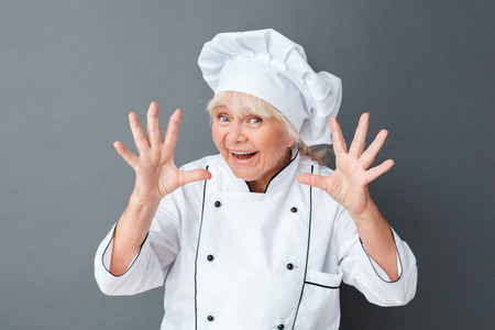 Senior woman chef studio standing isolated on gray frightening camera playful close-upの写真素材