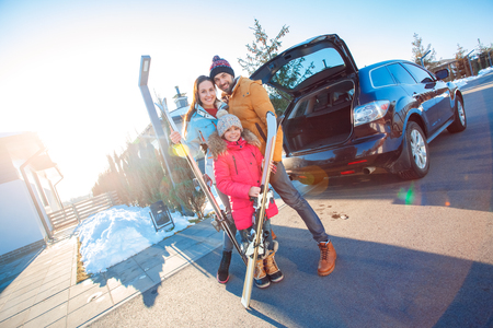 Winter vacation. Family time together outdoors standing hugging near car with skis smiling happyの写真素材
