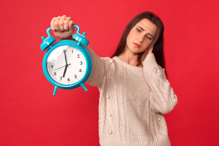 Freestyle. Young woman standing isolated on red with alarm clock blurred background dissatisfiedの写真素材