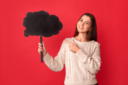 Freestyle. Young woman standing isolated on red pointing at cloud looking camera playfulの写真素材