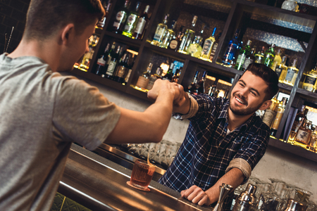 Young bartender standing at bar counter with customer fist bumb cheerfulの写真素材