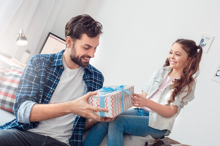 Father and little daughter at home sitting man holding present from daughter surprisedの写真素材