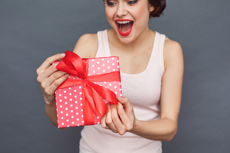 Special Day. Woman standing isolated on grey with gift close-up shouting surprisedの写真素材