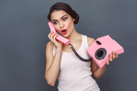 Freestyle. Woman standing isolated on grey talking on stationary phone excitedの写真素材