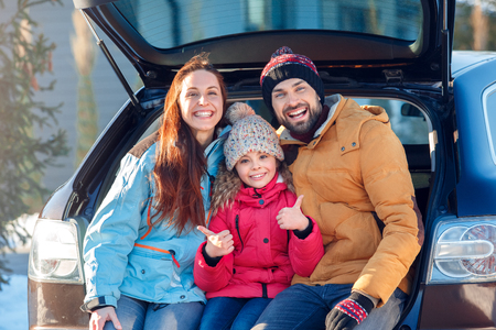 Winter vacation. Family time together outdoors standing sitting at car trunk laughing playful gitl showing thumb up close-upの写真素材