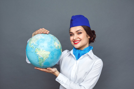 Professional Occupation. Stewardess standing isolated on grey showing globe looking camera cheerful close-upの写真素材