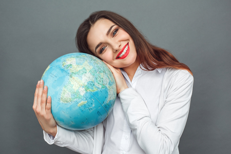 Freestyle. Woman standing isolated on grey hugging globe smiling cheerfulの写真素材