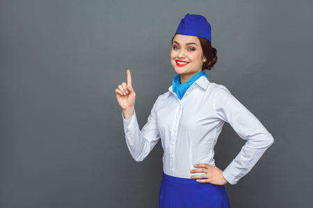Professional Occupation. Stewardess standing isolated on grey pointing up solution looking camera cheerfulの写真素材