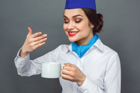 Professional Occupation. Stewardess standing isolated on grey smelling coffee smiling joyful close-upの写真素材