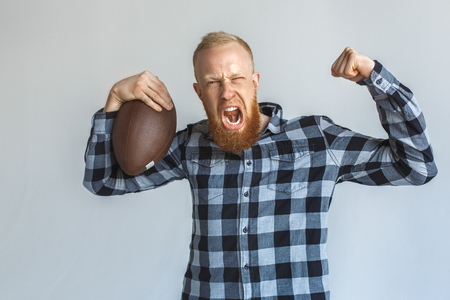 Strength. Mature man standing isolated on grey with ball showing biceps shouting close-upの写真素材
