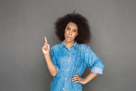 Mulatto woman standing isolated on grey pointing up looking camera sassyの写真素材