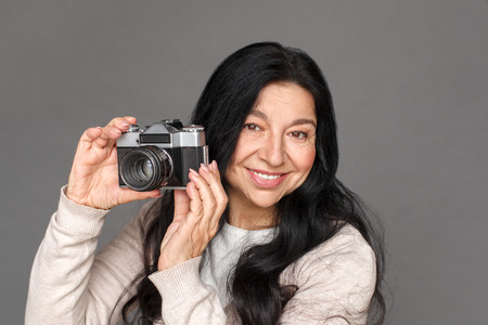 Photographer. Mature lady standing isolated on grey taking pictures with film camera cheerful...
