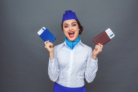 Professional Occupation. Stewardess standing isolated on grey hands aside with passports and tickets shouting cheerfulの写真素材