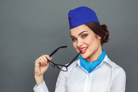 Professional Occupation. Stewardess standing isolated on grey biting eyeglasses looking camera playfulの写真素材