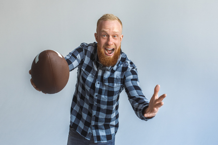 Freestyle. Mature man standing isolated on grey catching ball shouting cheerful close-upの写真素材