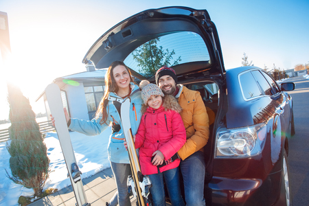 Winter vacation. Family time together outdoors standing sitting at car trunk with skis smiling cheerfulの写真素材