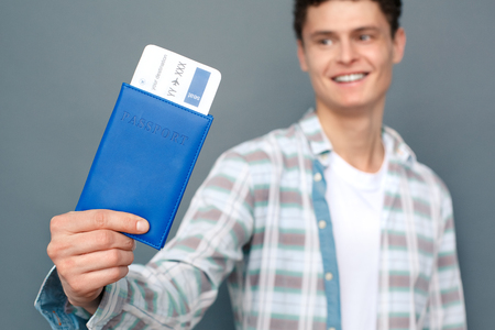 Man isolated on gray wall tourism concept standing holding passport with ticket close-up smiling blurredの写真素材
