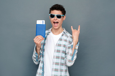 Man in sunglasses isolated on gray wall tourism concept standing holding passport and ticket posing coolの写真素材