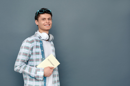 Man isolated on gray wall tourism concept standing carrying dictionary joyfulの写真素材