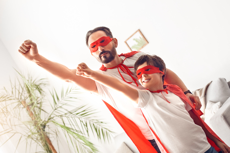 Father and son in hero costumes at home standing hands up flying excitedの写真素材