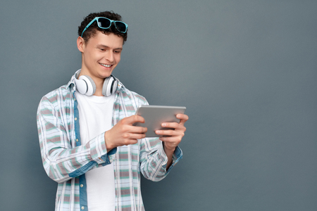 Man wearing headphones isolated on gray wall tourism concept standing playing game on digital table cheerfulの写真素材
