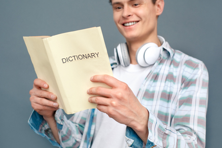 Man isolated on gray wall tourism concept standing reading dictionary happy close-upの写真素材