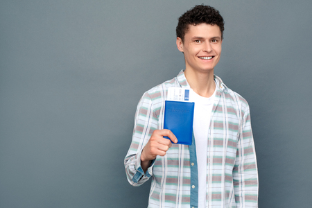 Man isolated on gray wall tourism concept standing looking camera happy holding passport with ticketの写真素材