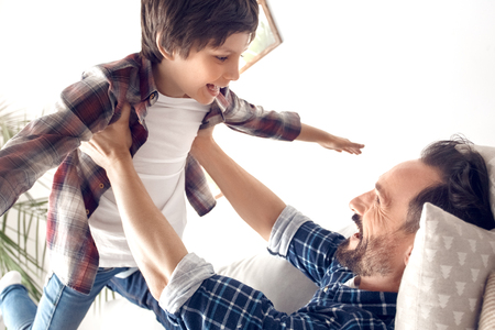 Father and little son at home lying on sofa dad making boy fly happy close-upの写真素材
