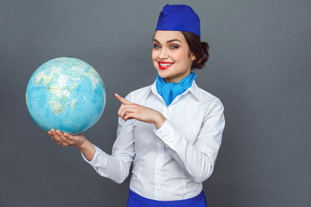 Professional Occupation. Stewardess standing isolated on grey pointing at destination on globe smiling happyの写真素材