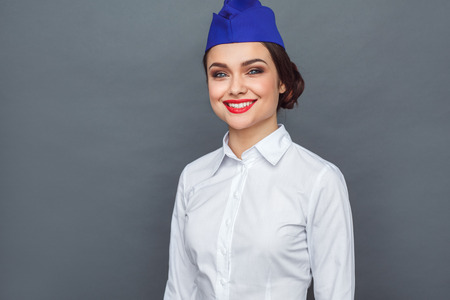 Professional Occupation. Stewardess standing isolated on grey looking camera cheerful close-upの写真素材