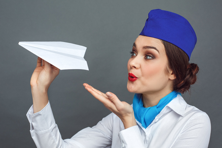 Professional Occupation. Stewardess standing isolated on grey blowing at paper plane smiling excited close-upの写真素材