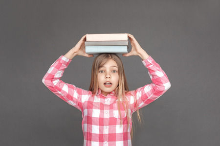 Freestyle. Girl standing isolated on grey with pile of books up looking camera surprisedの写真素材