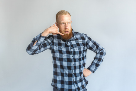 Freestyle. Mature man standing isolated on grey showing call gesture talking thoughtfulの写真素材