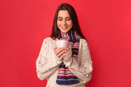 Freestyle. Young woman wearing scarf standing isolated on red looking at cup of milk smiling happyの写真素材