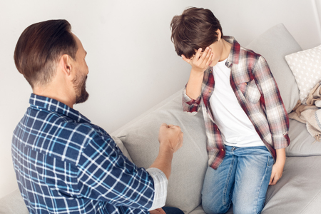 Father and little son at home sitting on sofa playing rockâpaperâscissors boy lostの写真素材