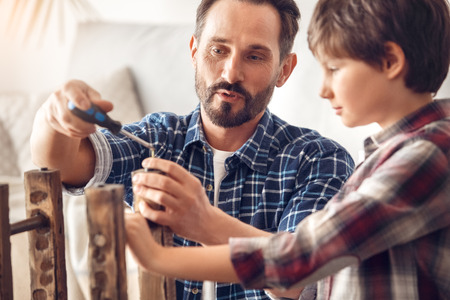 Father and little son at home standing dad holding screwdriver explaining boy process serious close-upの写真素材
