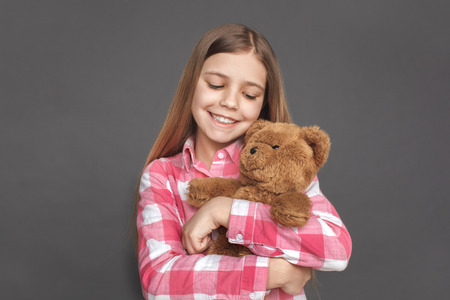 Freestyle. Girl standing isolated on grey hugging teddy bear happy close-upの写真素材