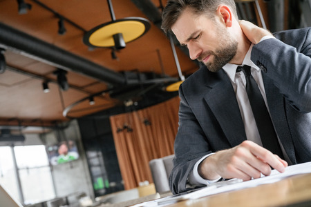Businessperson on business lunch at restaurant sitting touching neck muscle painの写真素材