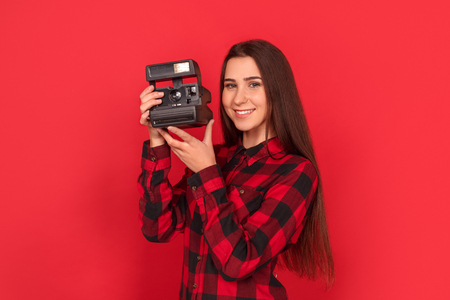 Photographer. Young woman standing isolated on red with instant camera smiling cheerfulの写真素材