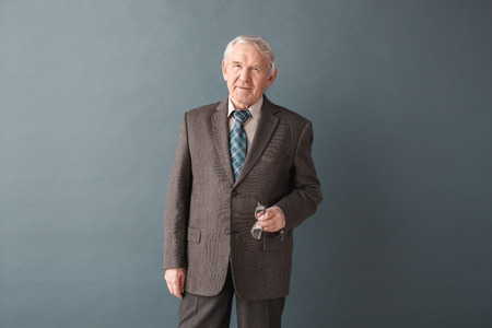 Senior man teacher studio standing isolated on gray holding glasses looking camera confidentの写真素材